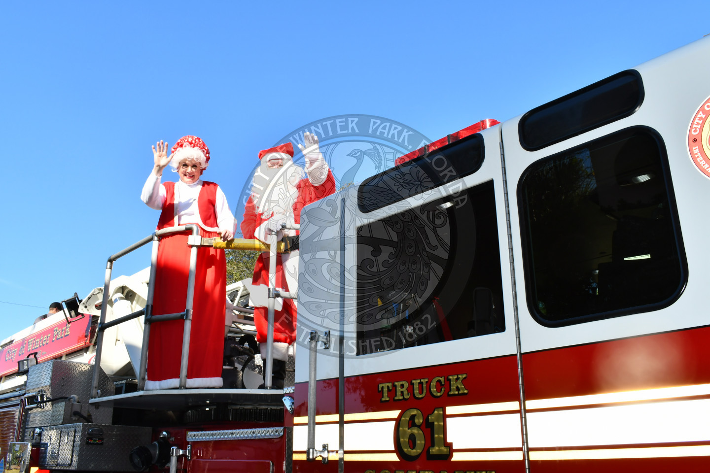 Mr. and Mrs. Claus on the top of a fire truck waving to the camera