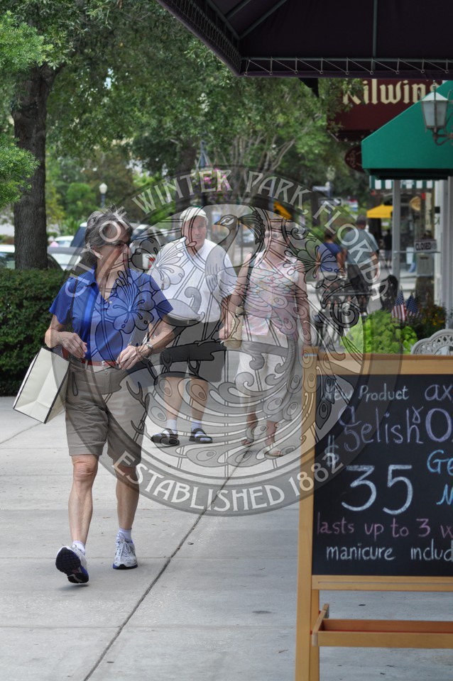 Three adult shoppers walking along the avenue as one of the female shoppers looks to her left with a shopping bag on her right sholder