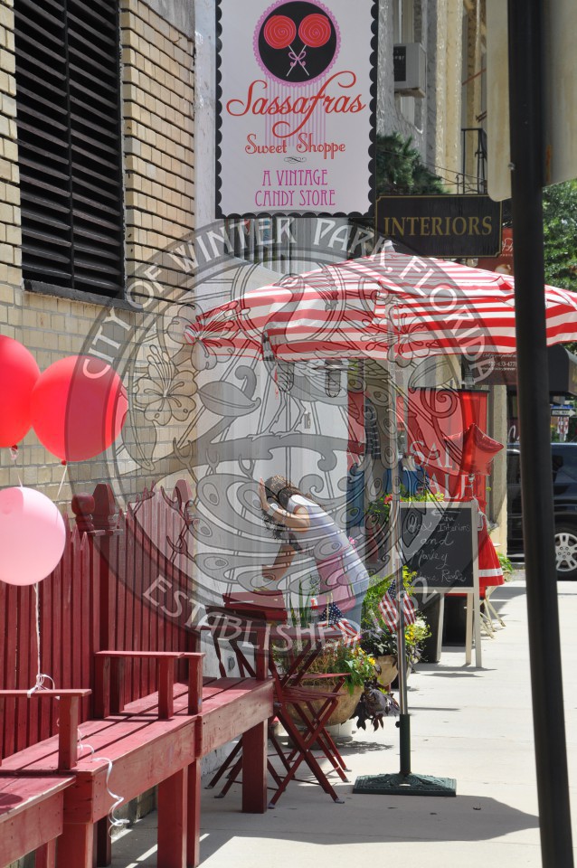 Red and white striped umbrella outside a storefront with a female wiping down one of the ledges