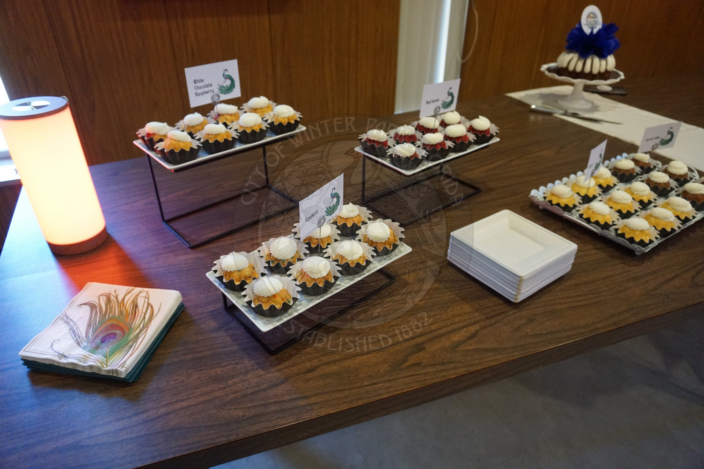 Capcakes on a table with napkins and plates between each plate of cupacakes. 