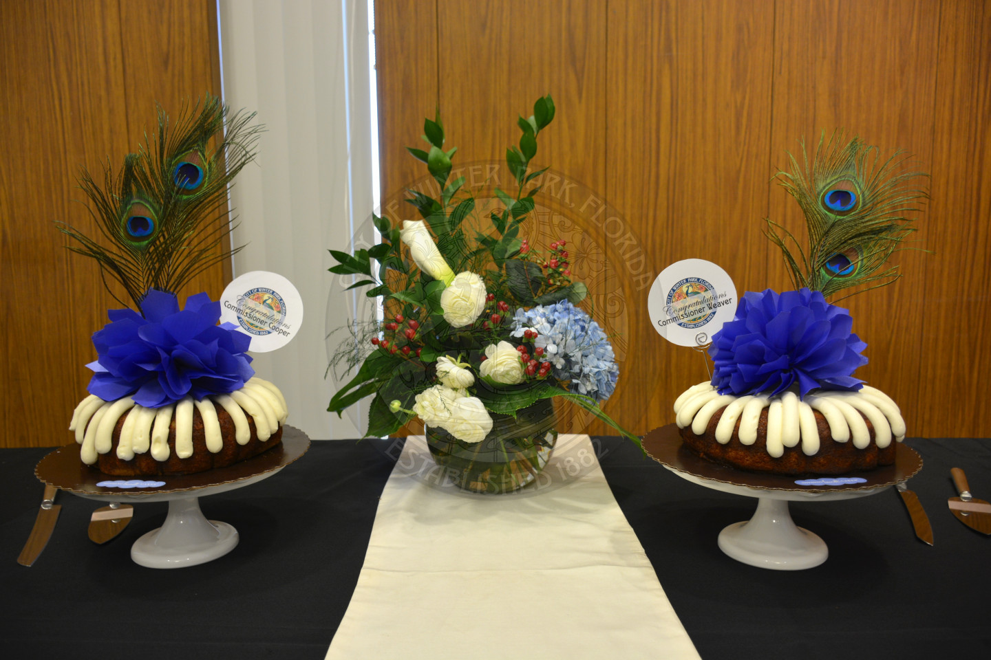 Two decorated bunt cakes on cake stands with beautiful flower arrangement placed in between the cakes.