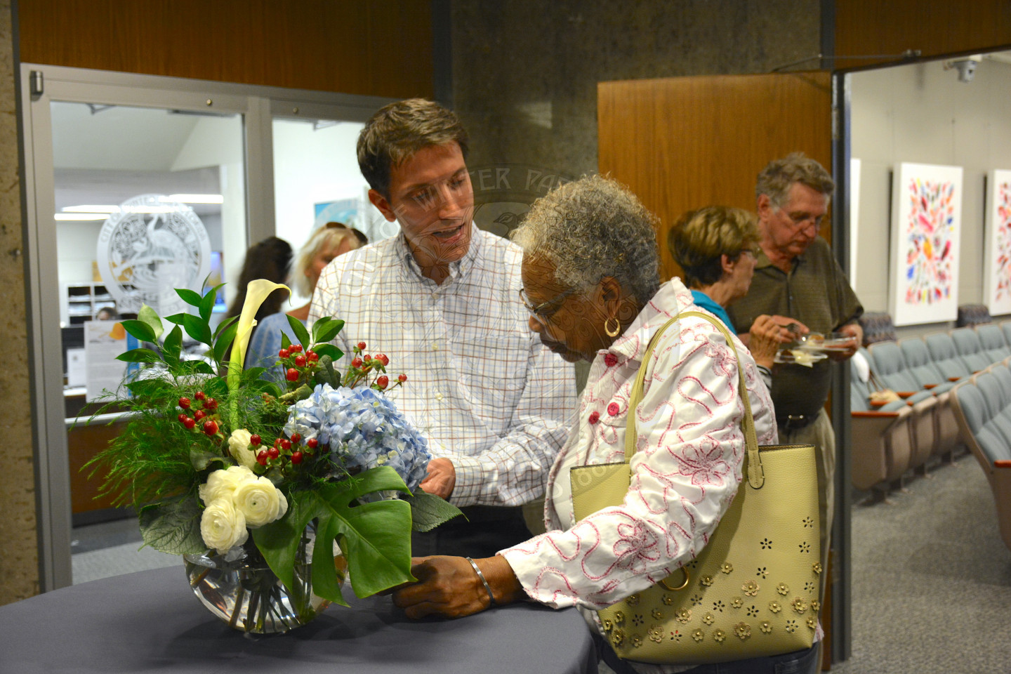 Male event attendee talks with female attendee at high-top table with a large floral centerpiece.