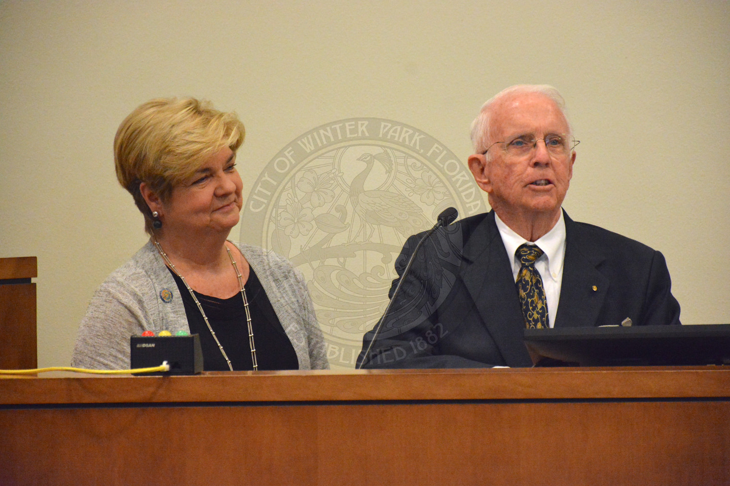 Cooper stands at podium as she recites her Oath of Office given by gentleman in a suit and tie.