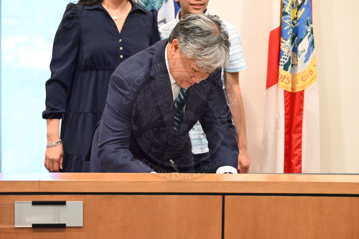 a man leaning down onto a table and signing a piece of paper.