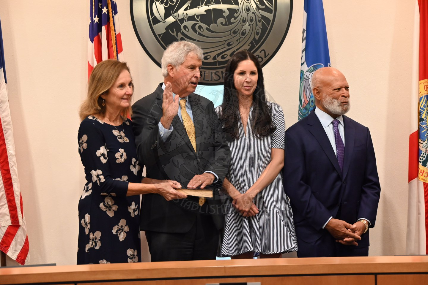 a man holding up his right hand with his left hand lays on a bible with his wife, daughter and a judge standing next to him.