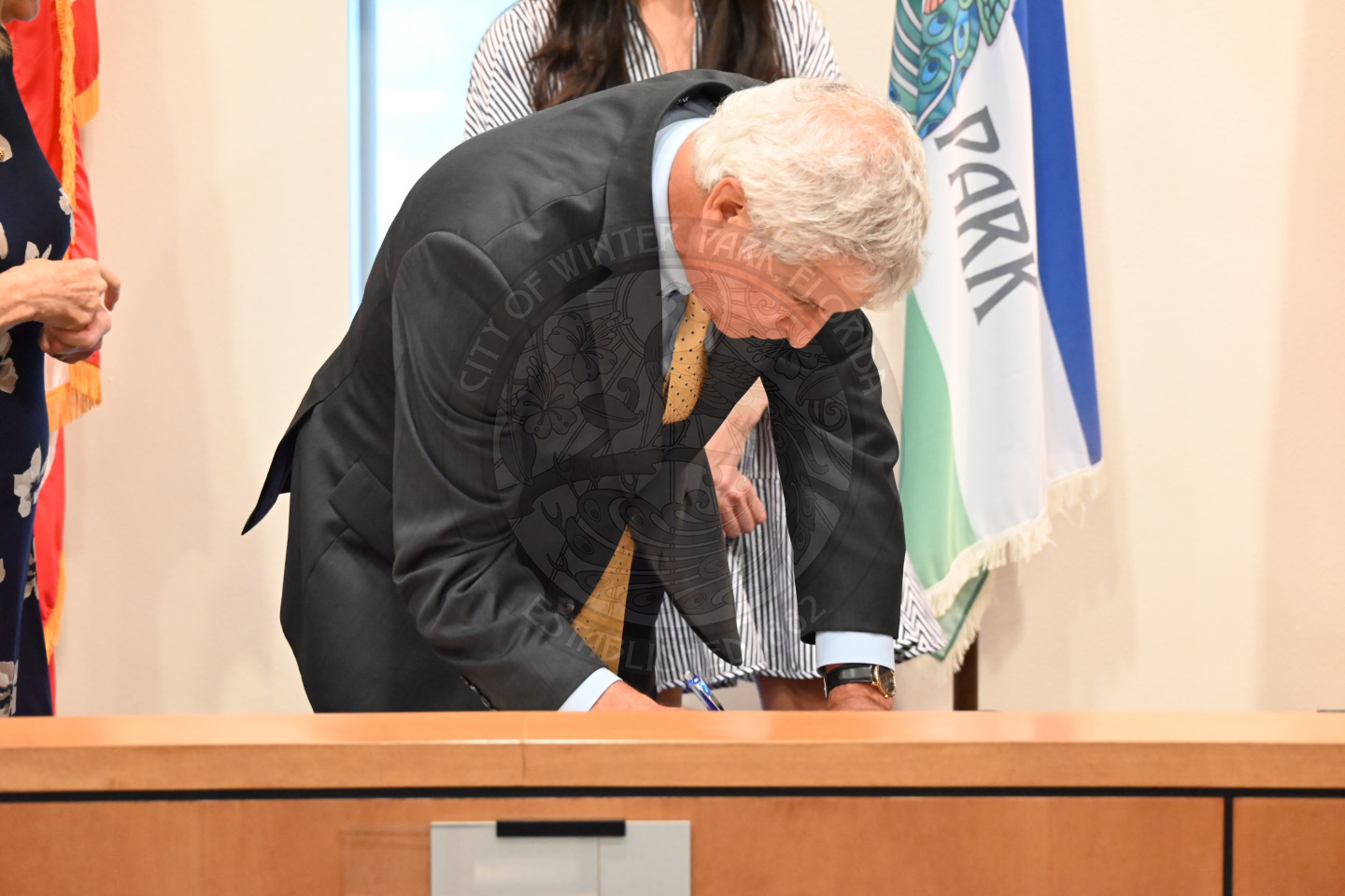 a man leaning down onto a table and signing a piece of paper.