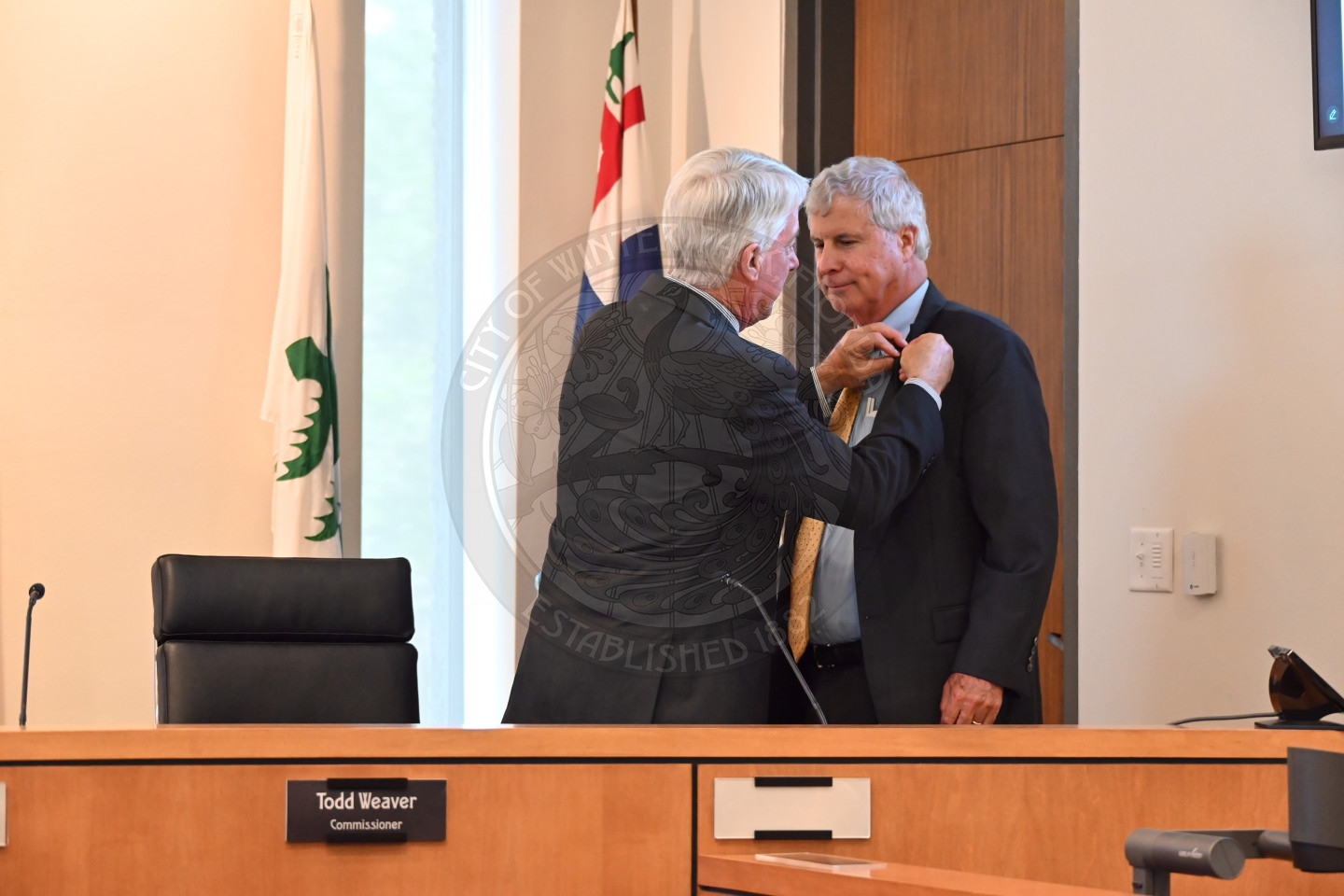 one man pinning a lapel pin on another man's jacket collar. 