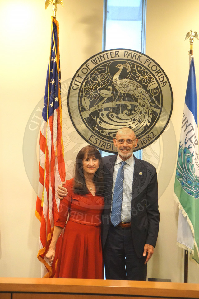Commissioner Sheila DeCiccio and her husband standing in front of the city seal and smiling for the camera