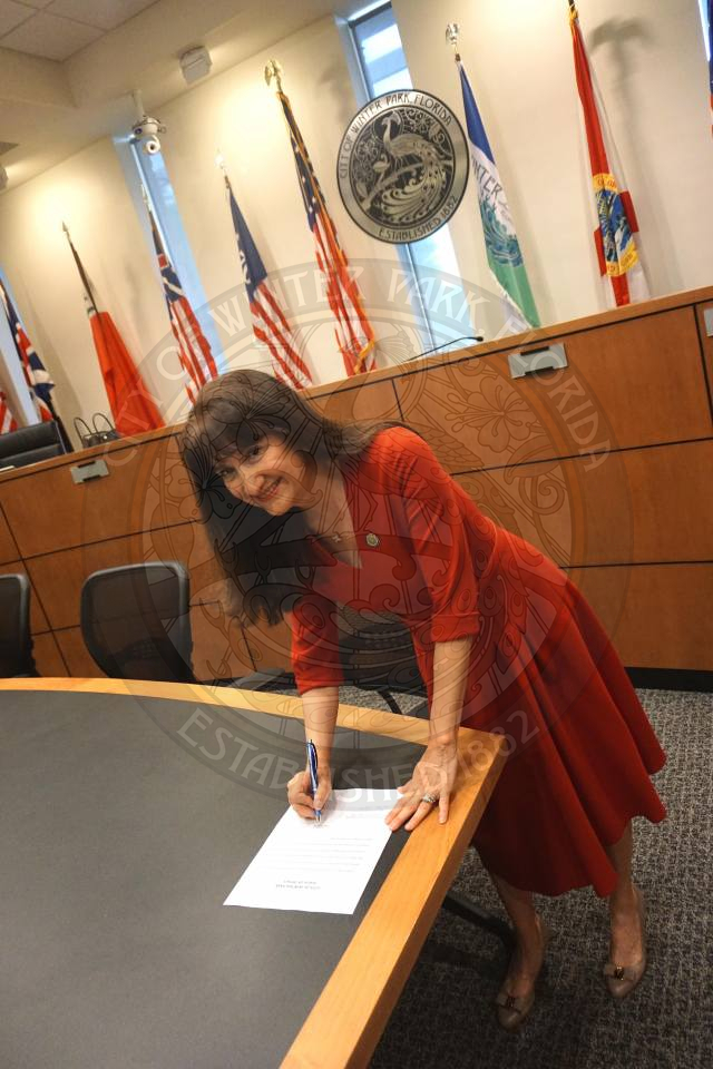 Commissioner Sheila DeCiccio signing offical paper and smiling at the camera