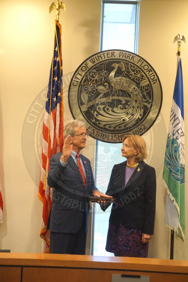 Commissioner Marty Sullivan holding his right hand up with his left hand on a bible that his wife is holding