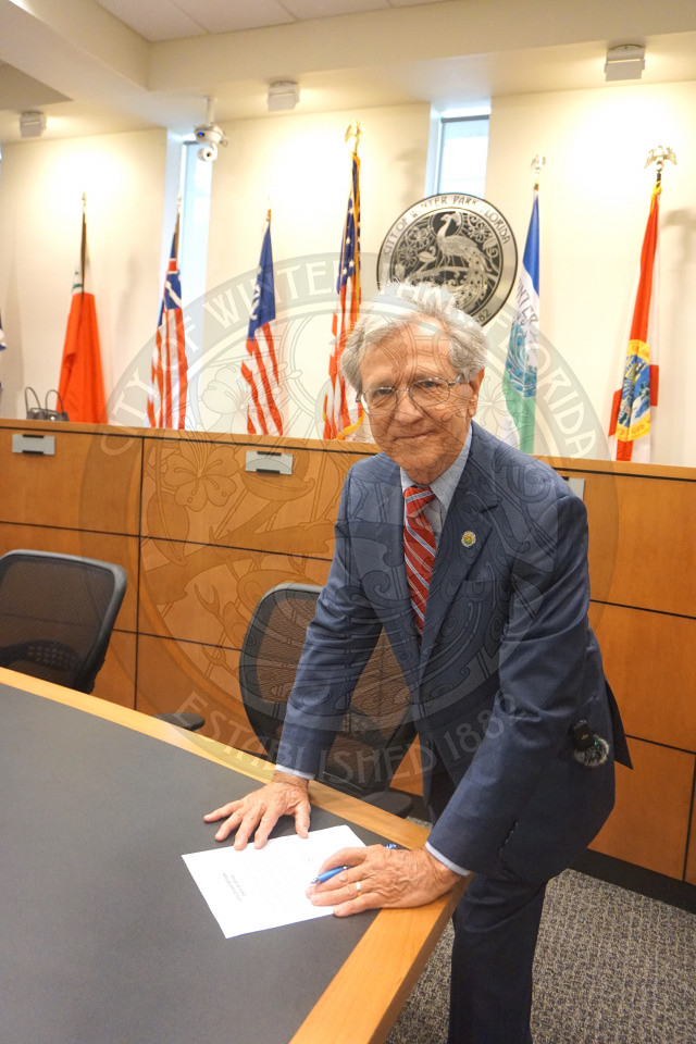 Commissioner Marty Sullivan signing offical paper and smiling at the camera