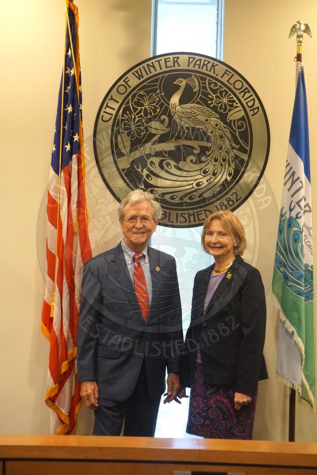 Commissioner Marty Sullivan and his wife standing in front of the city seal and smiling for the camera