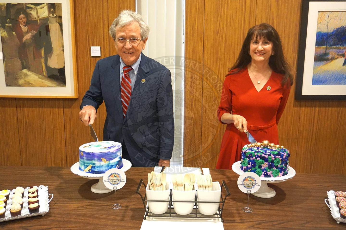 Commissioner DeCiccio and Sullivan standing behind their cakes and cutting into it while smiling for the camera