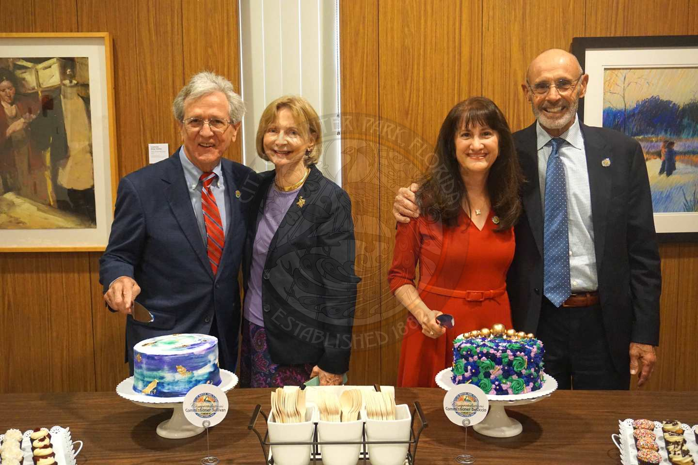 Commissioner Sullivan and his wife and Commissioner DeCiccio standing next to their spouses while standing behind a table with cakes on it smiling for the camera
