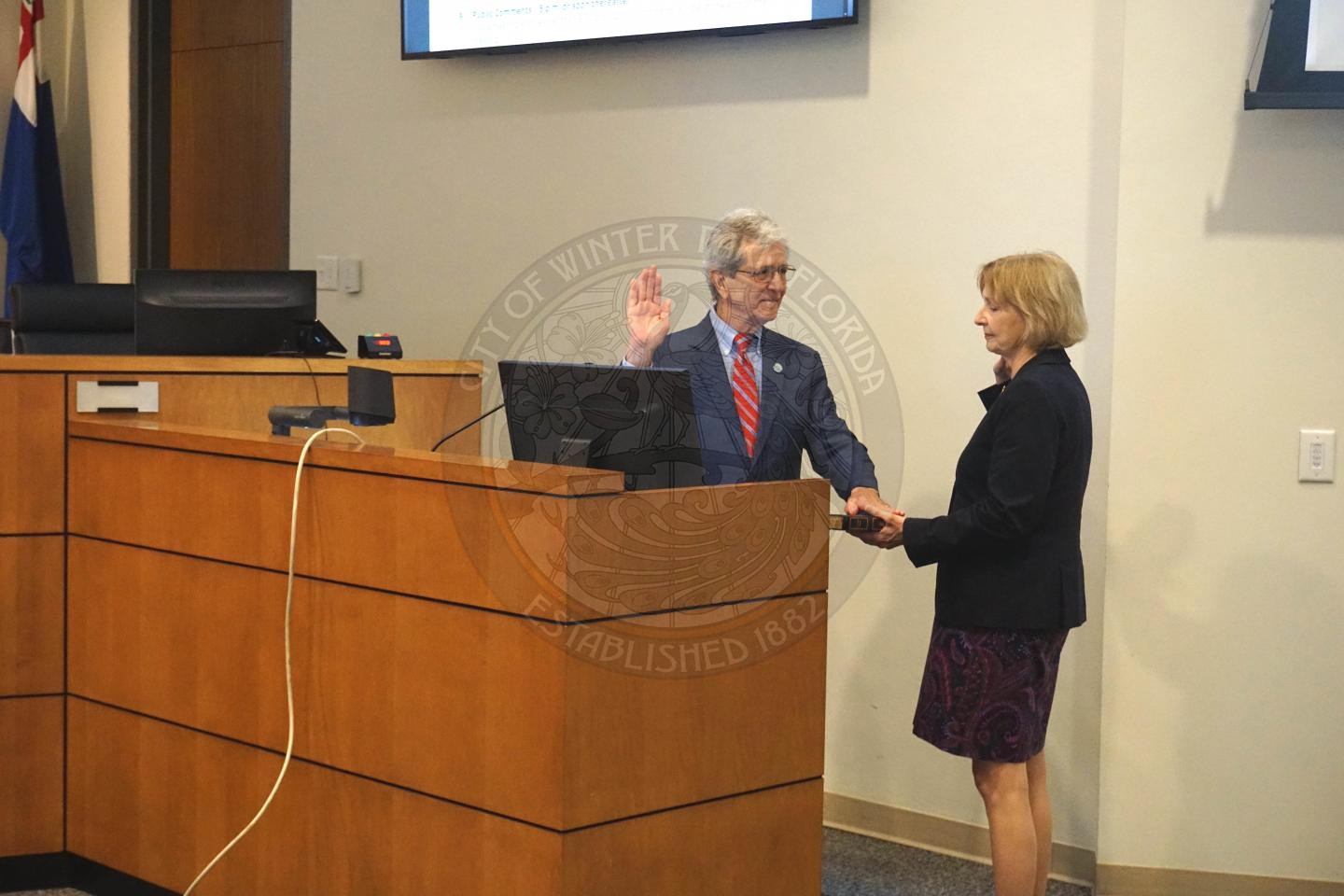 Commissioner Marty Sullivan holding his left hand on a bible that his wife is holding and holding his right hand up while he is swearing-in to office