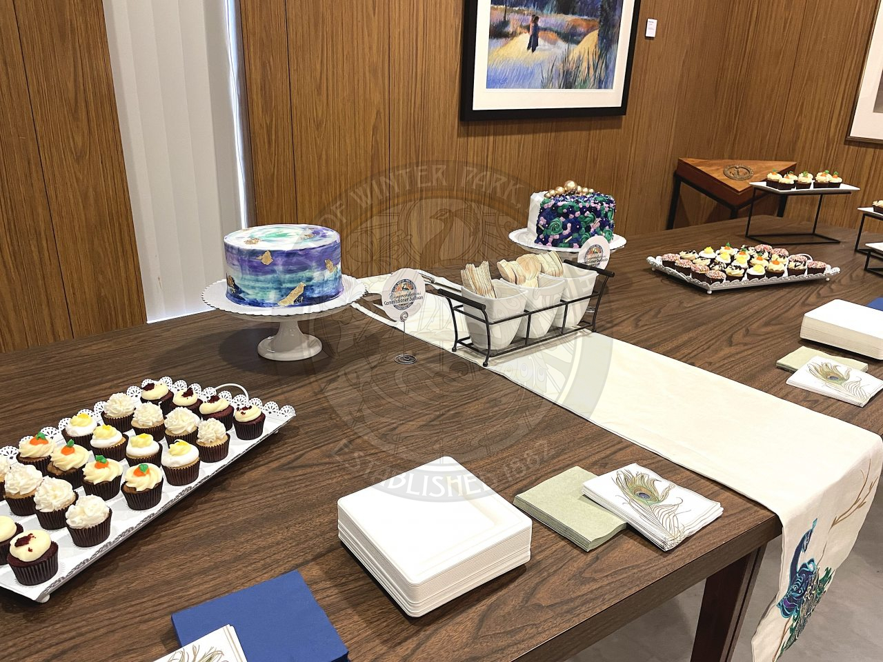 table with cakes, cupcakes, paper napkins, paper plates, and paper utensils