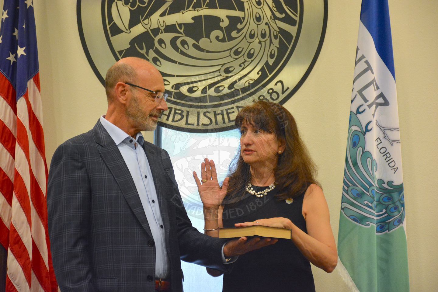 Commissioner DeCiccio raising her right hand with her left hand placed on a bible her husband is holding during her official swearing in ceremony