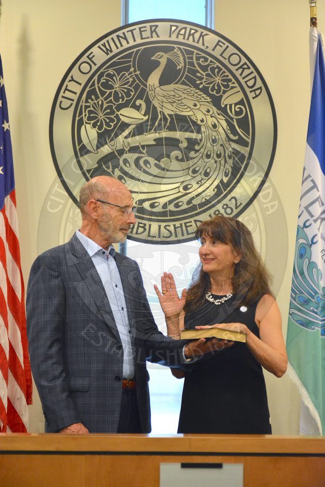 Commissioner DeCiccio raising her right hand with her left hand placed on a bible her husband is holding during her official swearing in ceremony