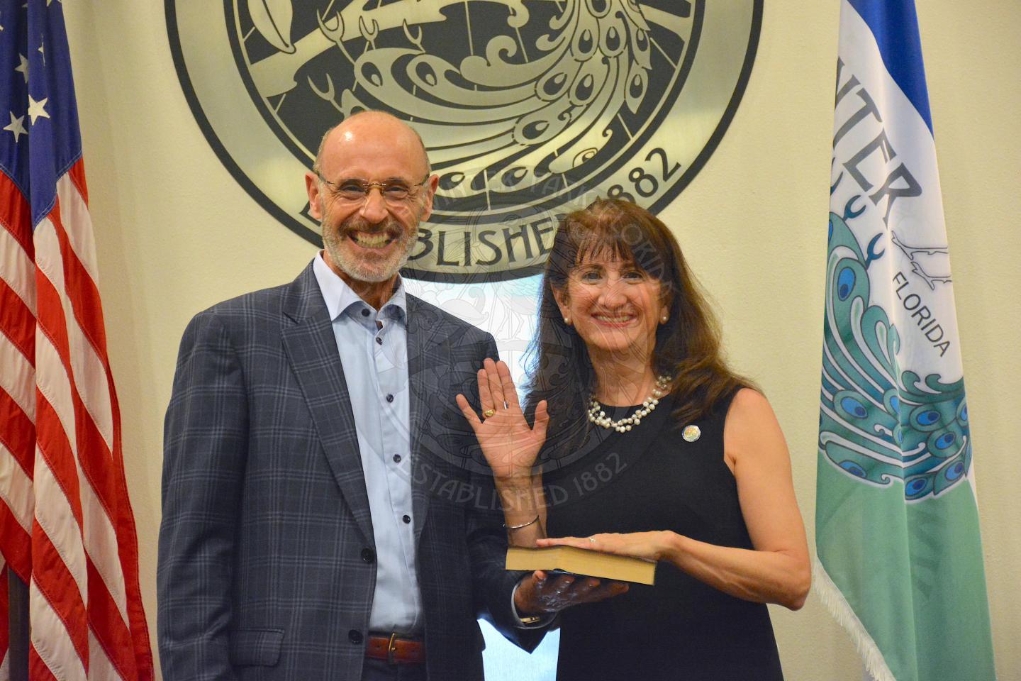 Commissioner DeCiccio raising her right hand with her left hand placed on a bible her husband is holding, both with big smiles after her official swearing in ceremony