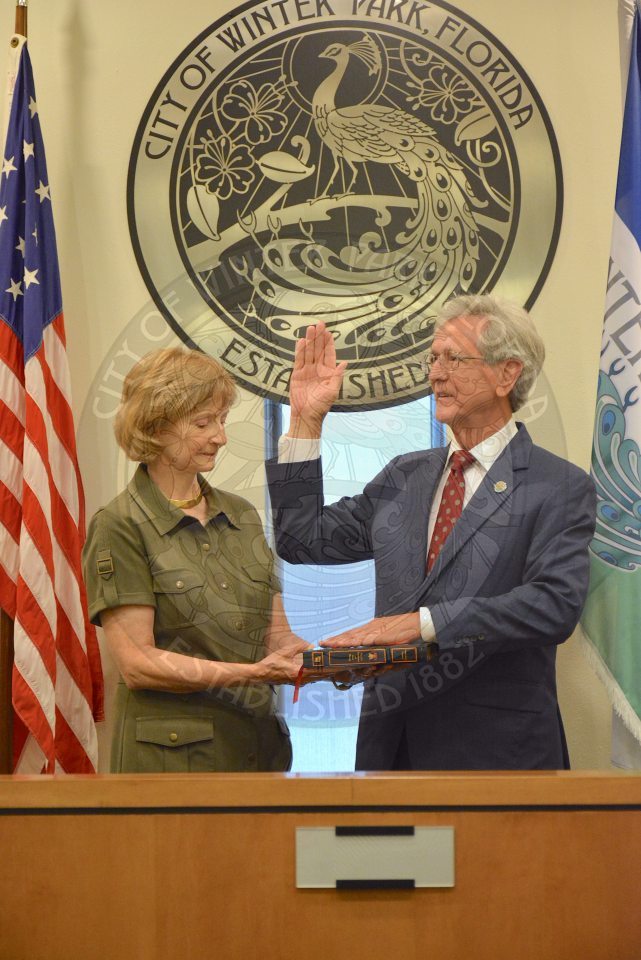 Commissioner Sullivan raising his right hand with his left hand placed on a bible his wife is holding during his official swearing in ceremony
