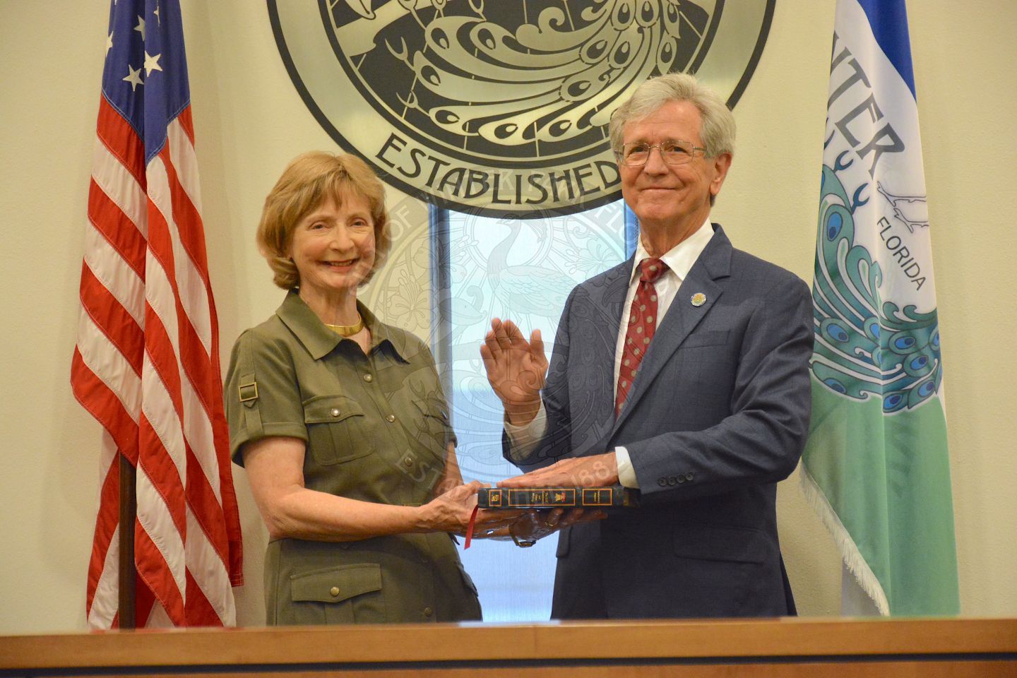 Commissioner Sullivan raising his right hand with his left hand placed on a bible his wife is holding, both with big smiles after his official swearing in ceremony