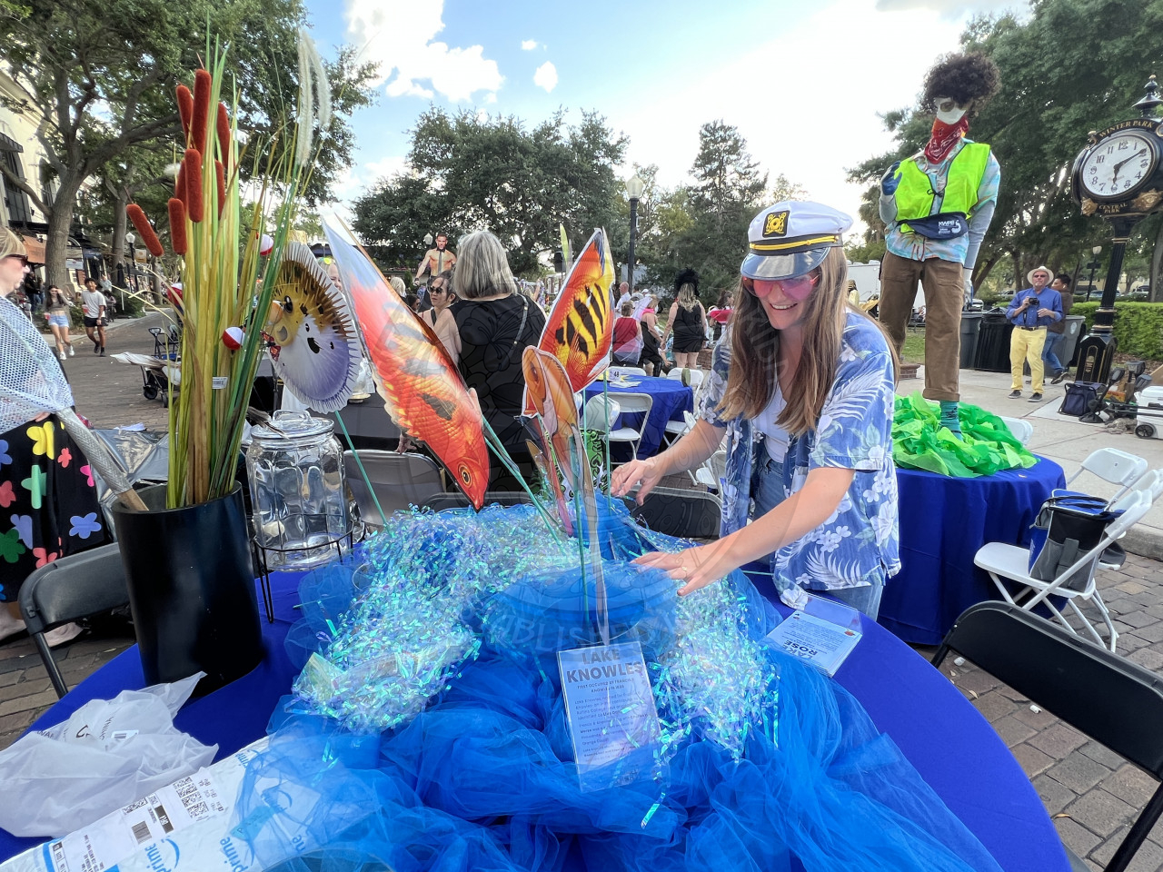 A woman decoraing their table to be a lake. There is blue tulle, confetti and a table cloth with moss. 
