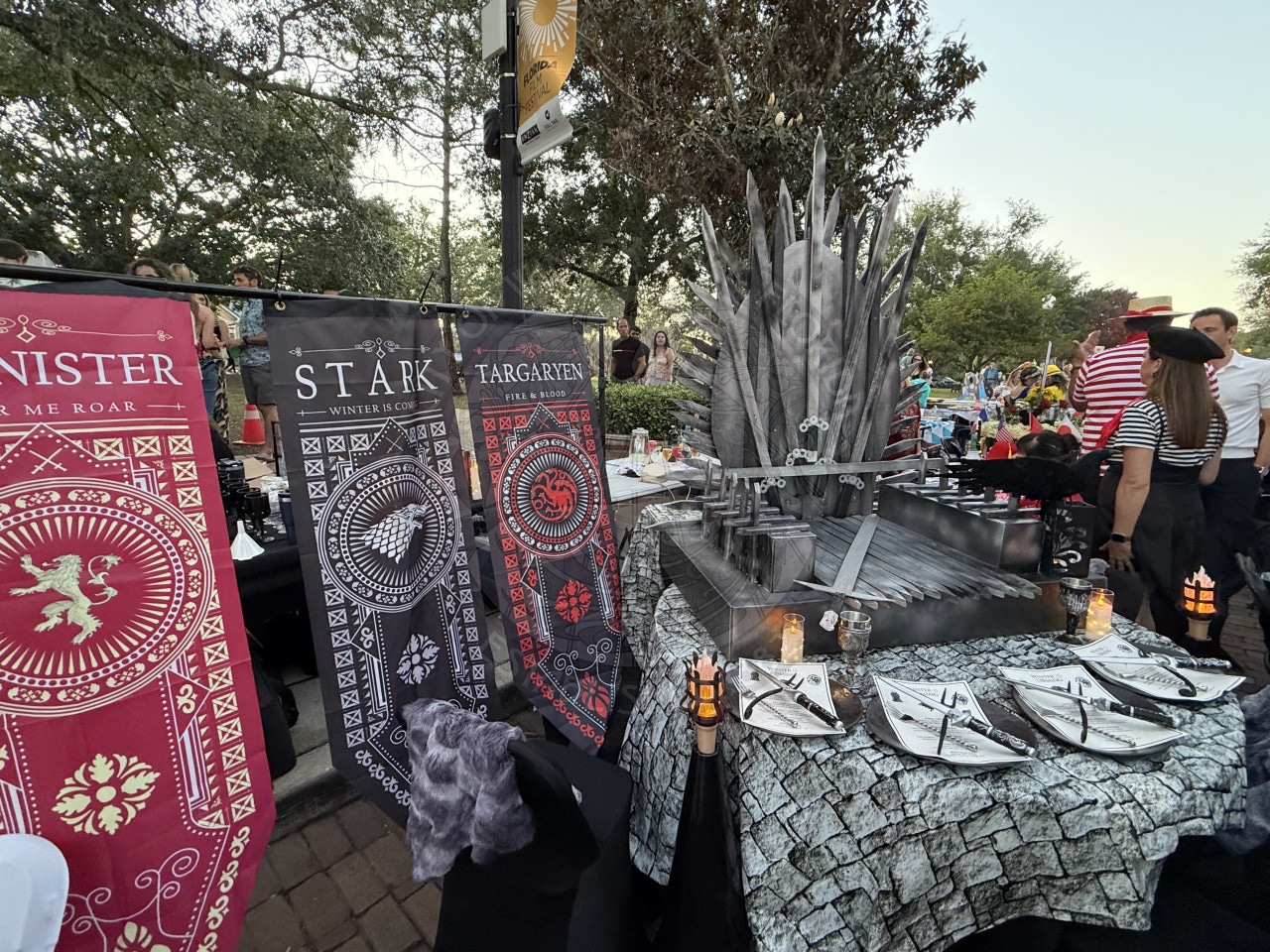 Game of Thrones-themed display with house banners and an Iron Throne centerpiece on a decorated table outdoors.
