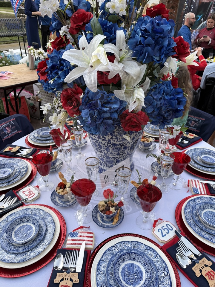 Blue and white plates with red accents on a table, centerpiece of red, white, and blue flowers, with an America250 patriotic theme.