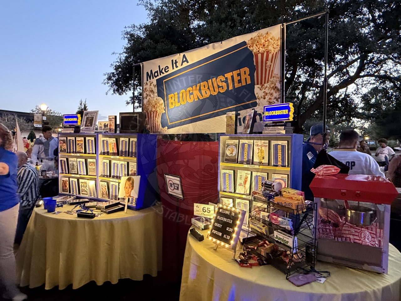 Blockbuster-themed booth display with VHS tapes, popcorn machine, and nostalgic movie decorations at an outdoor event.