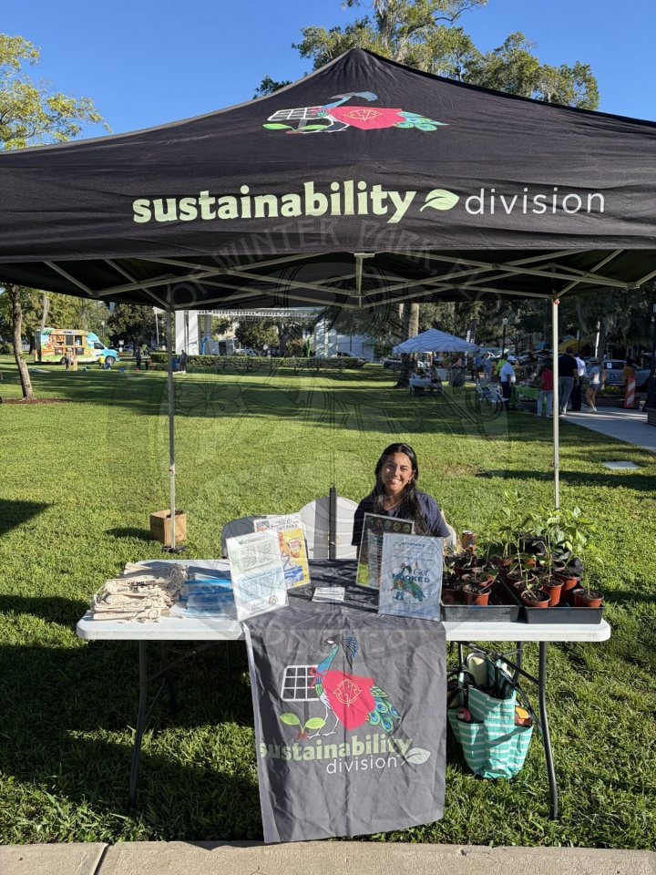 A woman sits at a sustainability division information booth in a park.