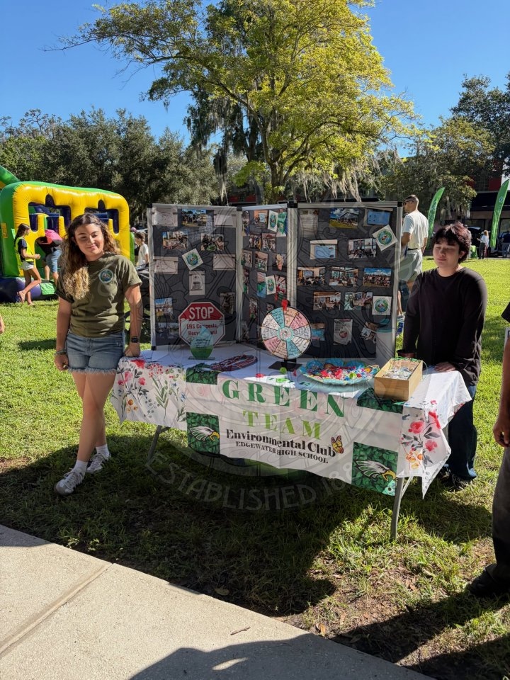 Two students stand behind a Green Team Environmental Club display table at an outdoor event.