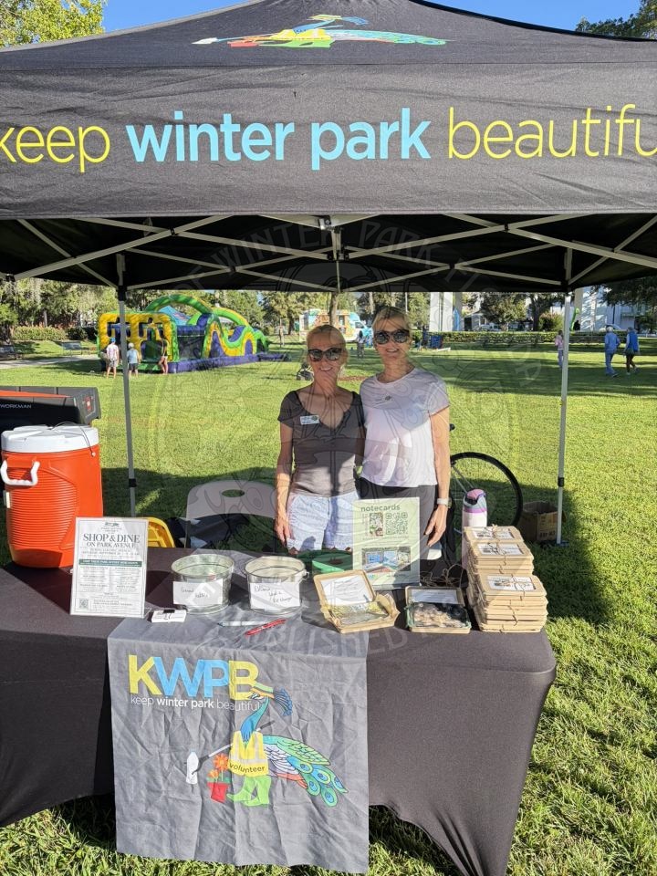 Two women stand behind a Keep Winter Park Beautiful information booth at a park.