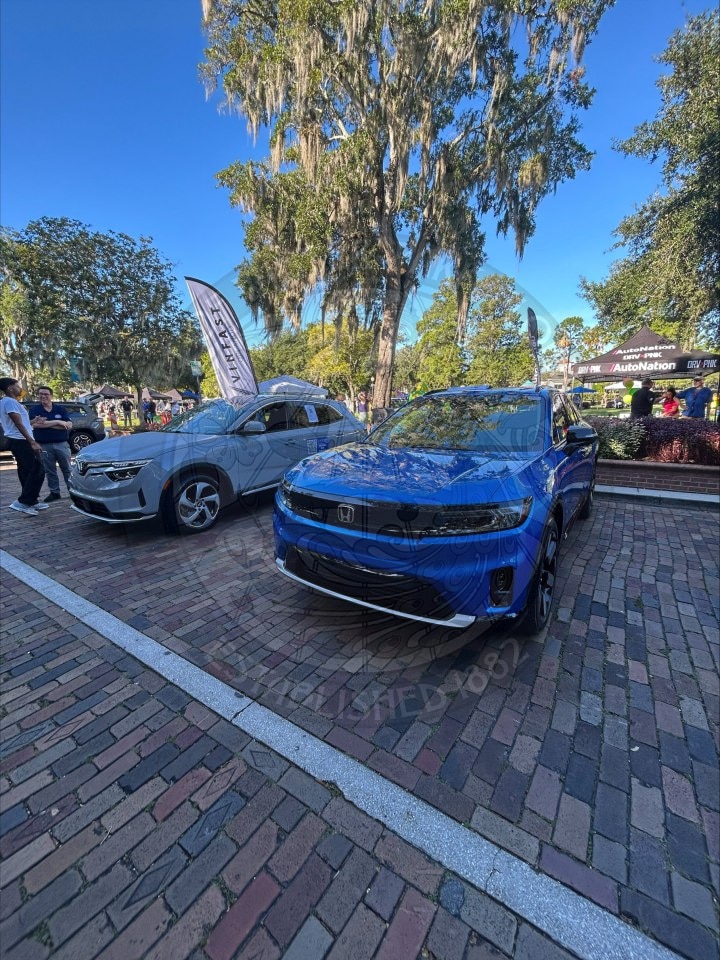 A blue Honda and a gray VinFast SUV parked on a brick street during an outdoor event.