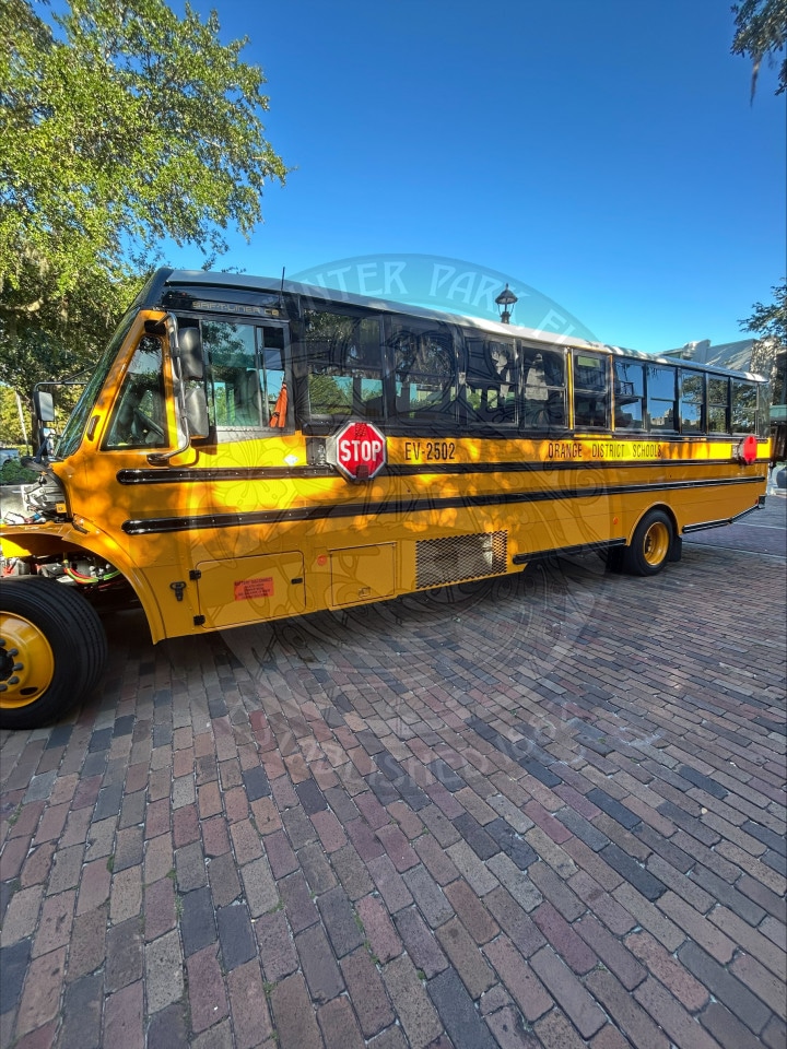 Yellow Orange EV District School bus parked on a brick street.