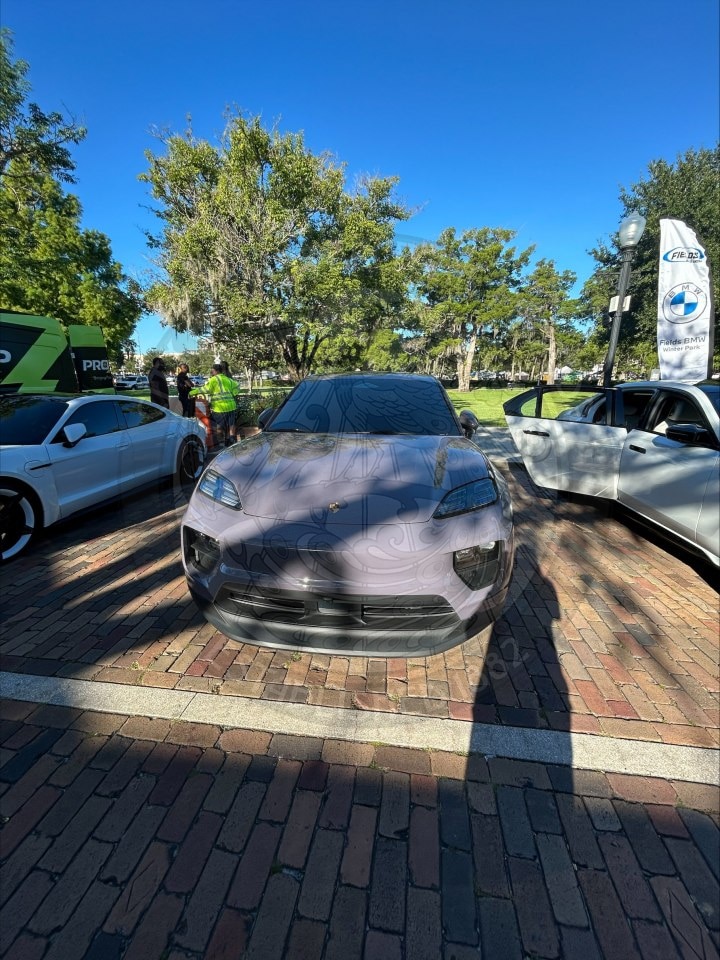 A light purple Porsche with a patterned hood parked on a brick plaza.