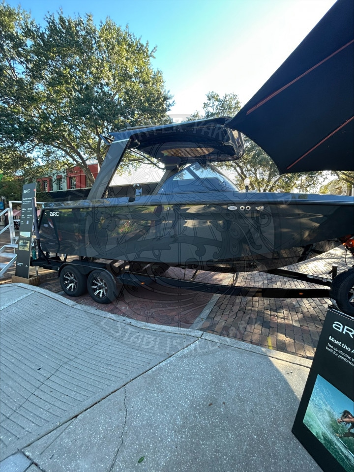 A dark gray Arc electric boat on a trailer parked outdoors, with signage nearby.