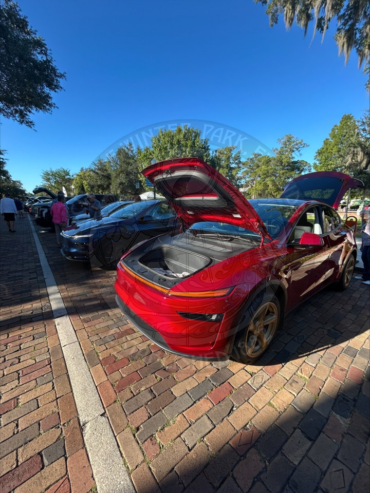 Red electric vehicle parked on a brick street with its front and rear trunks open.