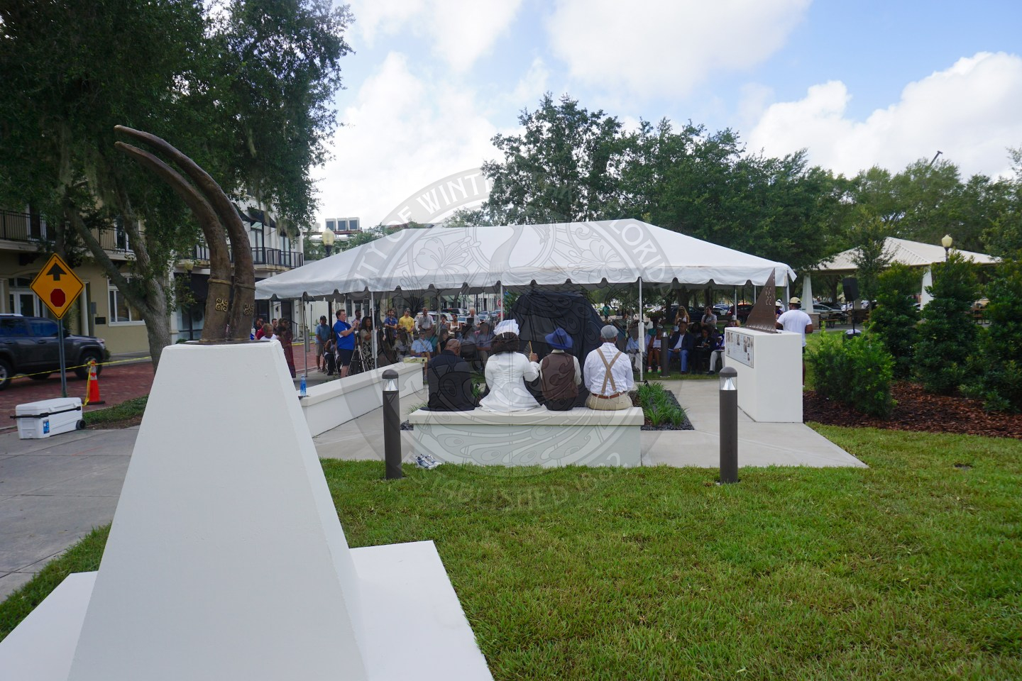 an overview of people sitting in chairs underneath the tent listening to the program.