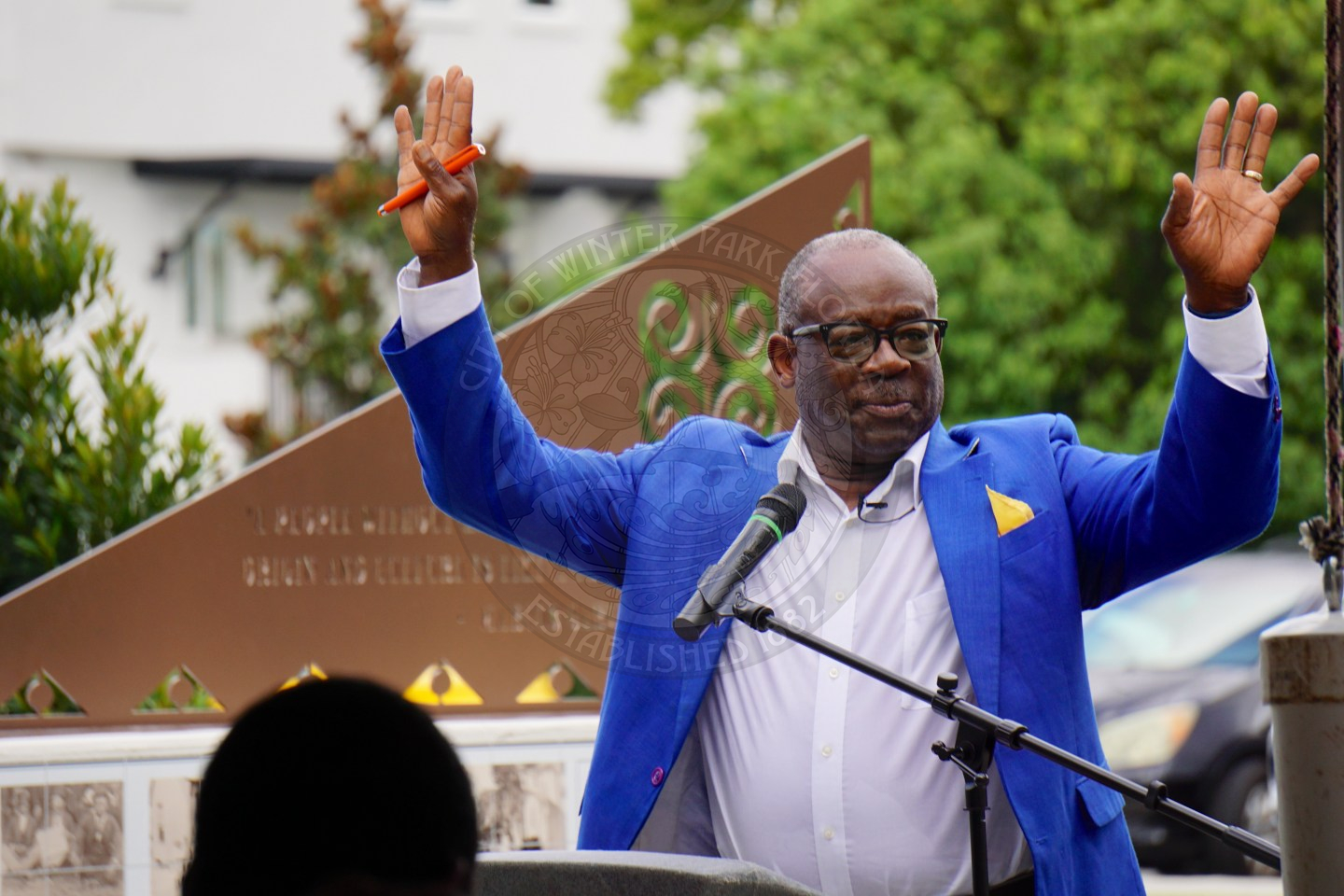 a man standing behind a podium raising both of his hands in the air while speaking.