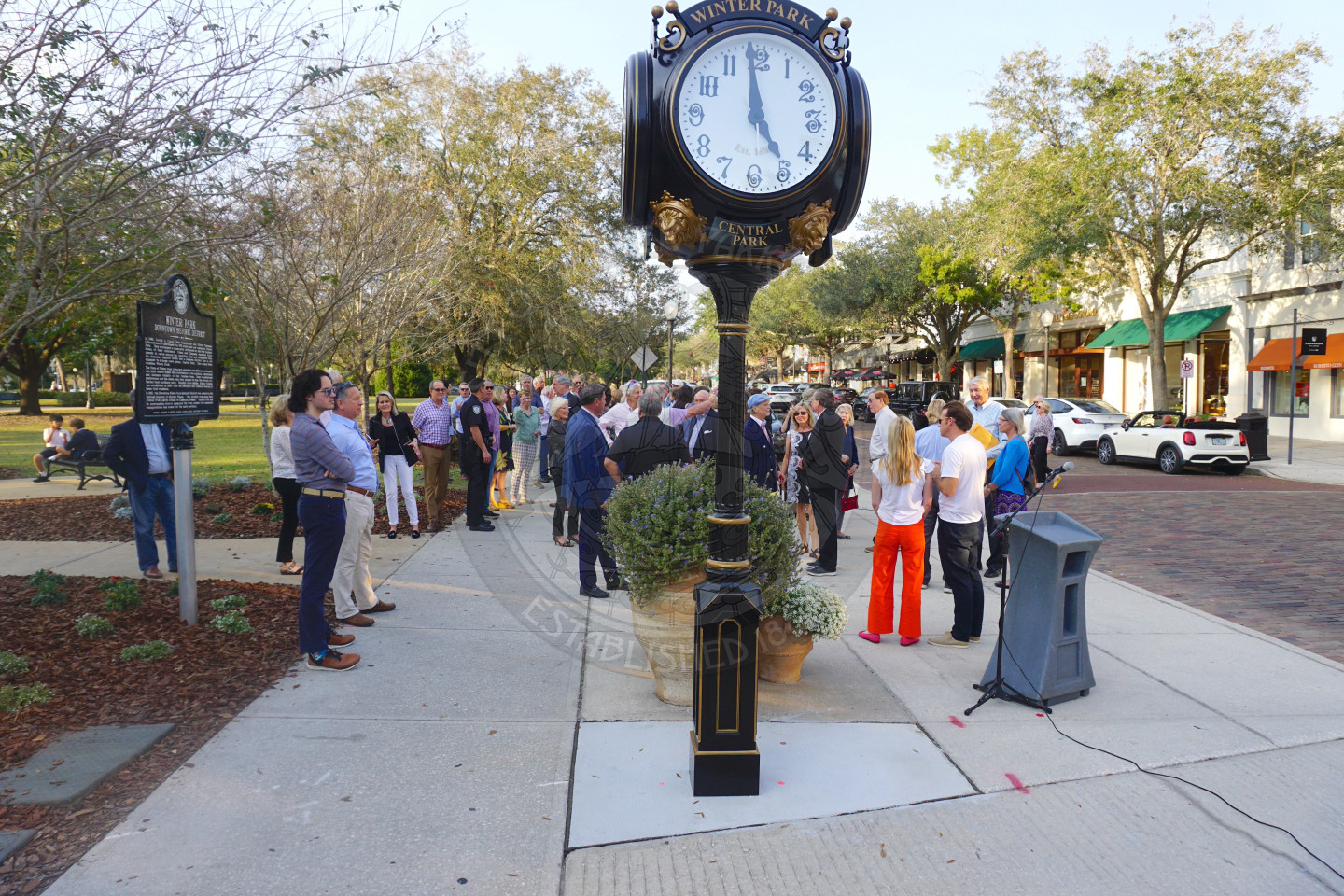 Full view of historic clock in Central Park with a group of people mingling.
