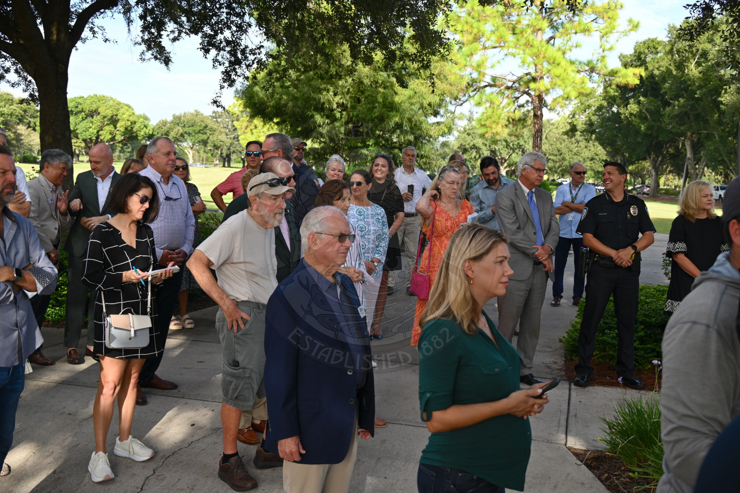 a bunch of people standing around watching someone talk about the dedication to the gateway sign