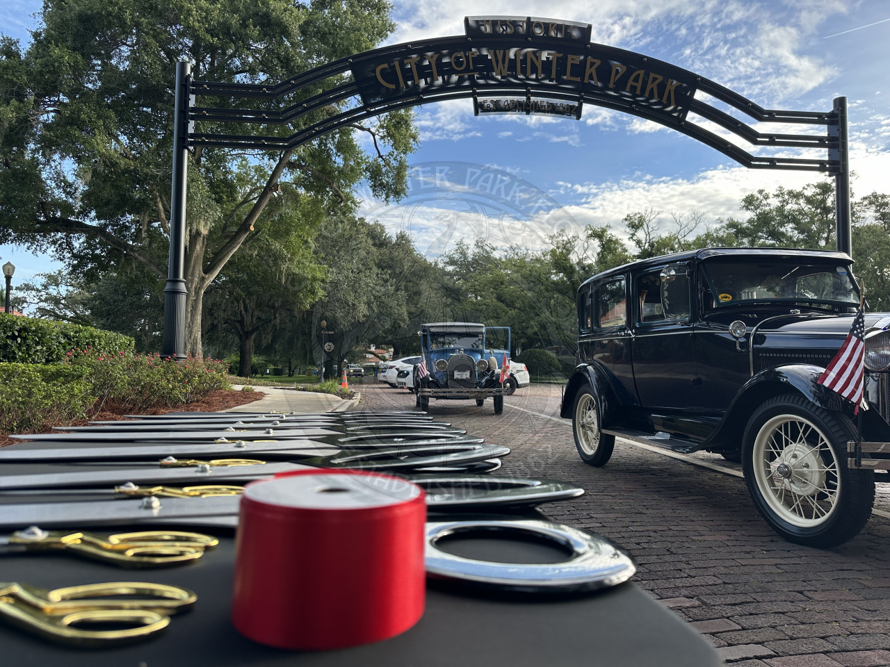 ribbon and scissors sitting on a table with old cars parked underneath the City of Winter Park gateway sign