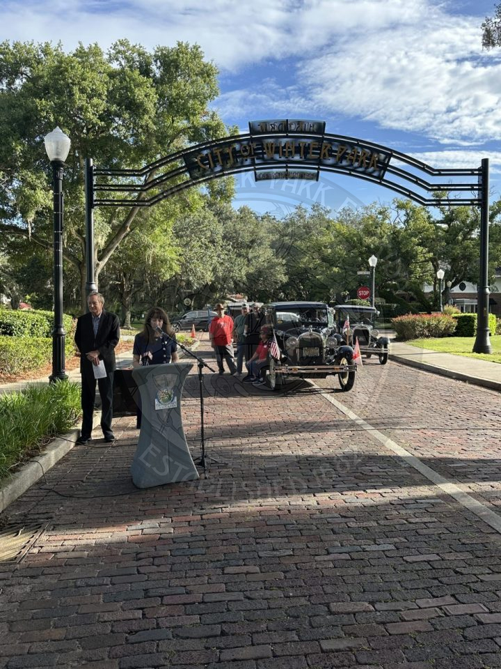 a woman standing behind the podium talking into a microphone in front of the gateway sign