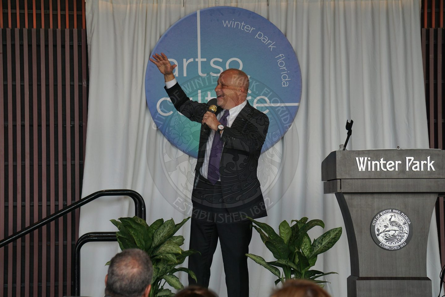 Man on a stage talking into a microphone with a podium to the left of him staying Winter Park