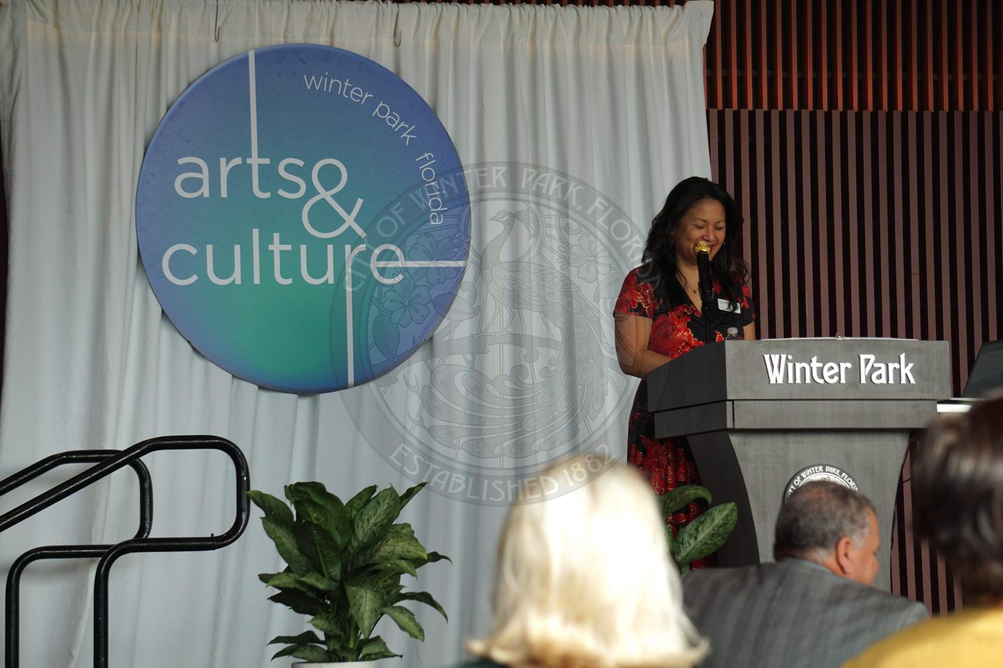 Woman standing behind the podium looking down on it while talking into microphone.
