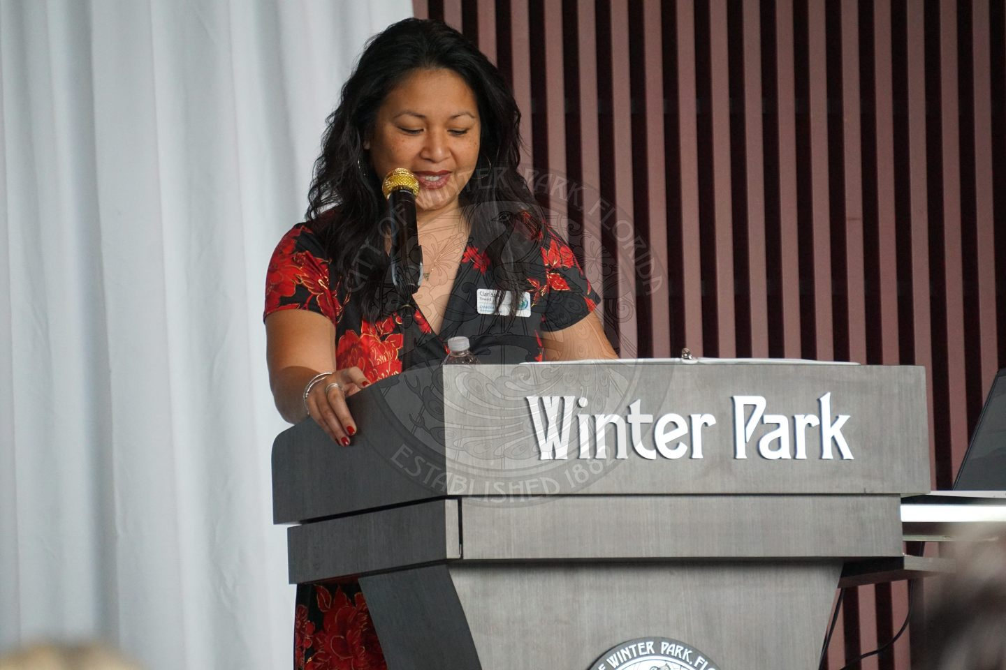 a women standing behind a podium that says 'Winter Park' and talking into a microphone
