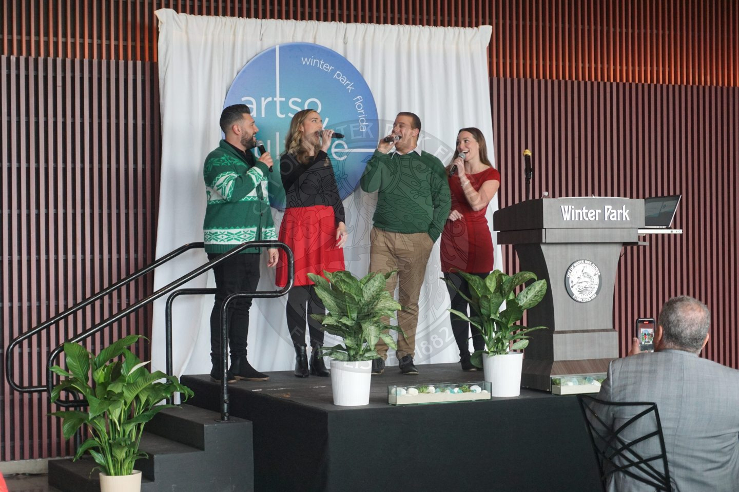 Group of two women and two men singing into micorphones on a stage.