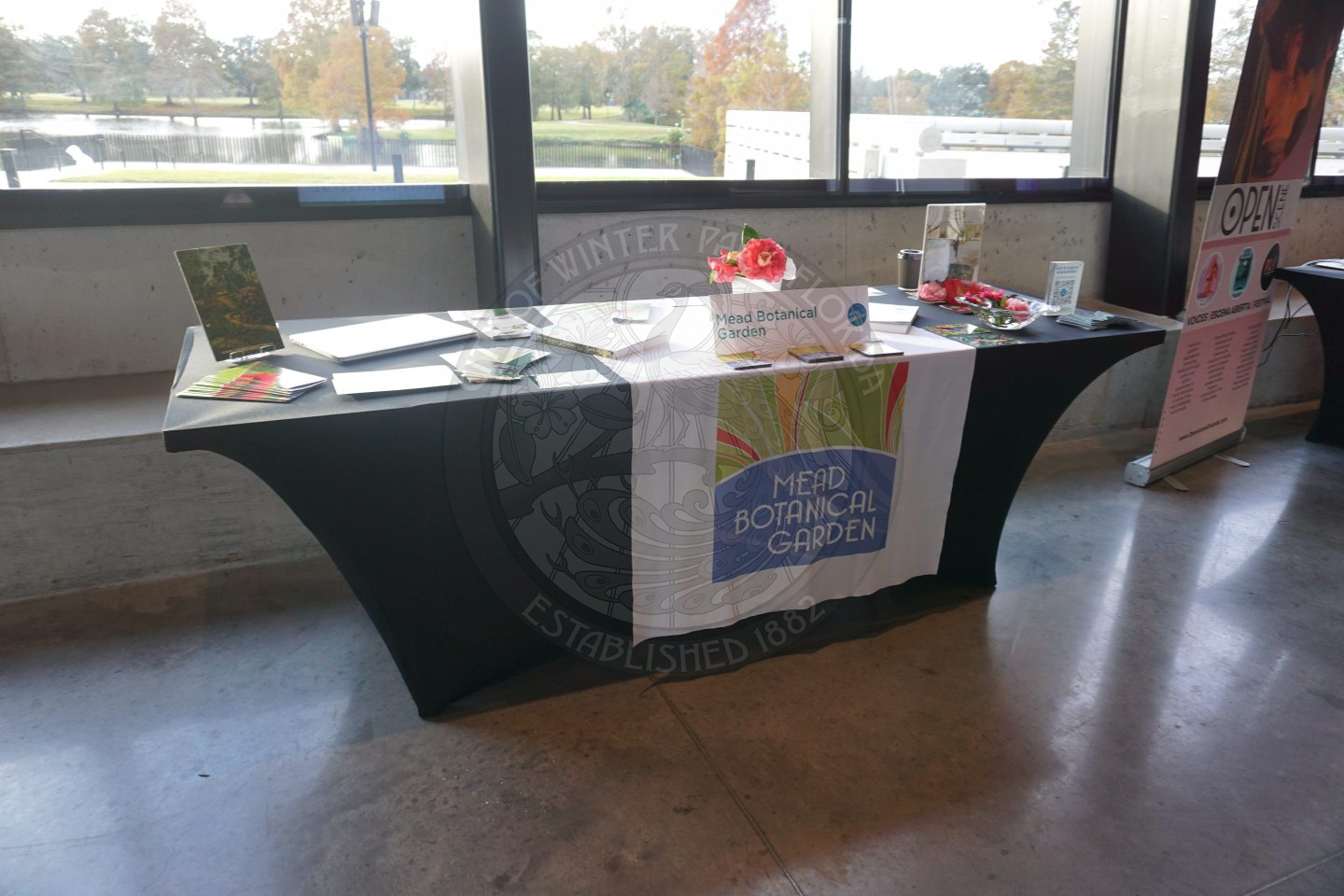 A table with black linen and on top of the black linen is a table runner that states Mead Botanical Garden and papers surrounding it regarding information about the company.
