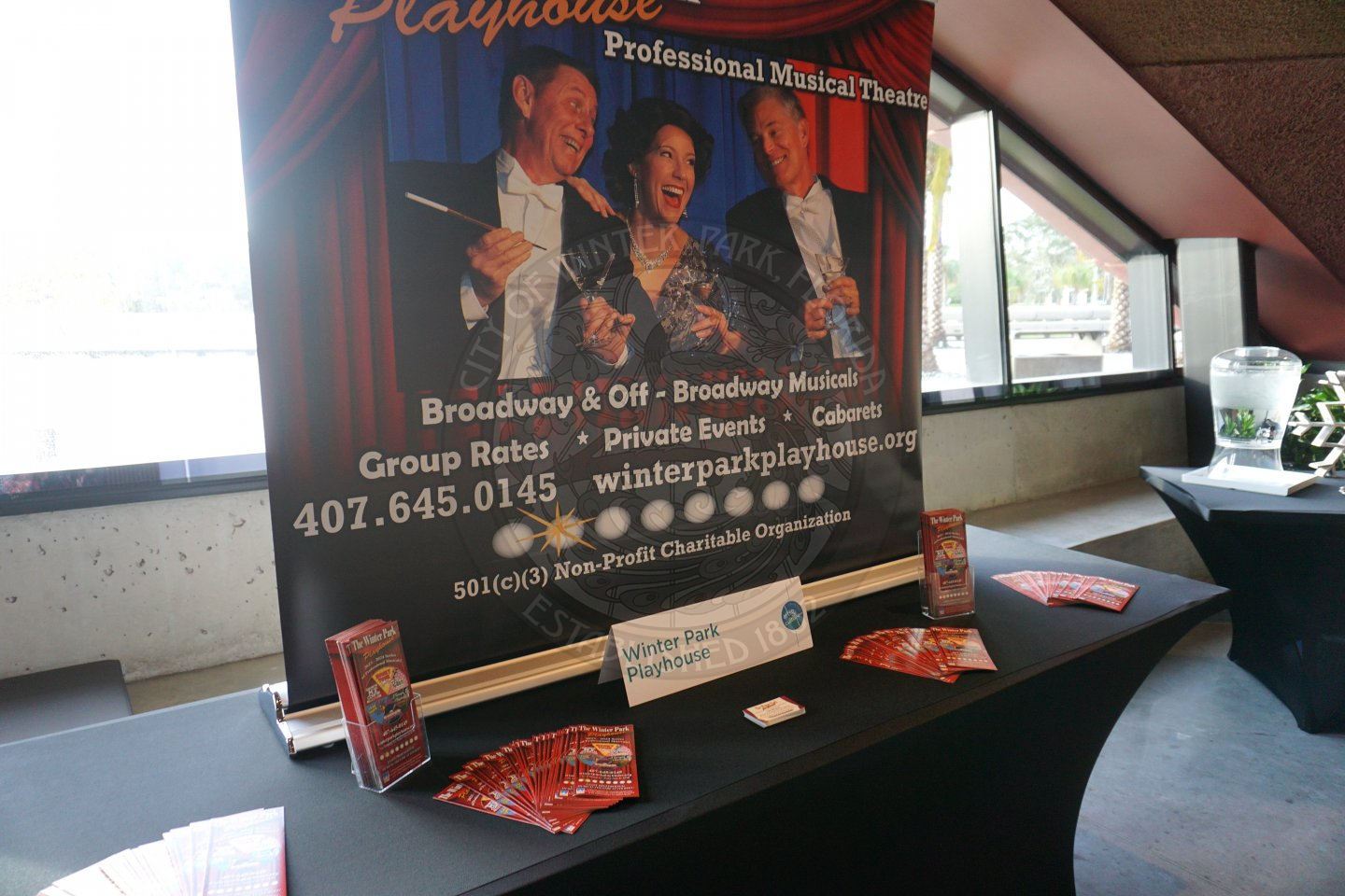 an 8 foot table with black linen with Winter Park Playhouse pamplets and picture. 