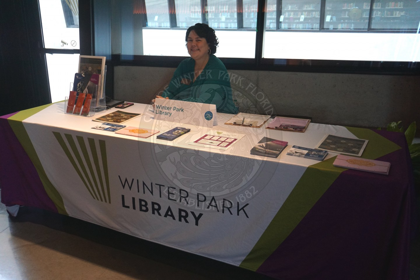 A lady sitting behind a table that has information about Winter Park Library.